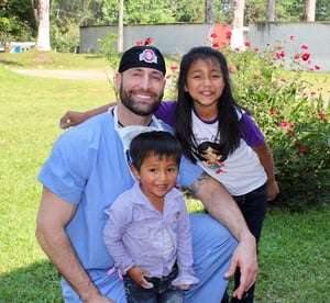 Dr. Justin Gusching kneeling next to smiling children in Guatemala during the HELPS International medical mission trip